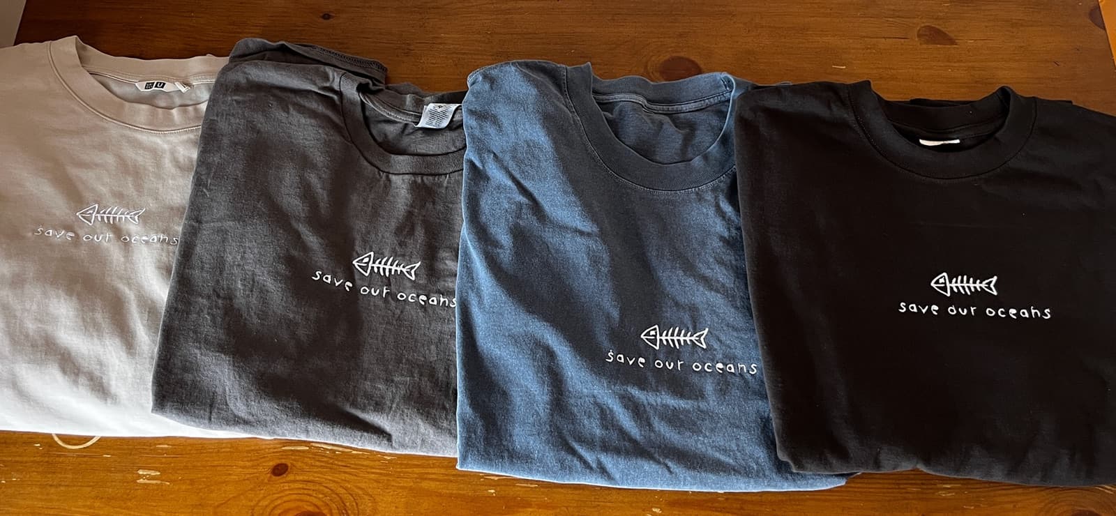Four embroidered secondhand t-shirts laid out on a wooden table