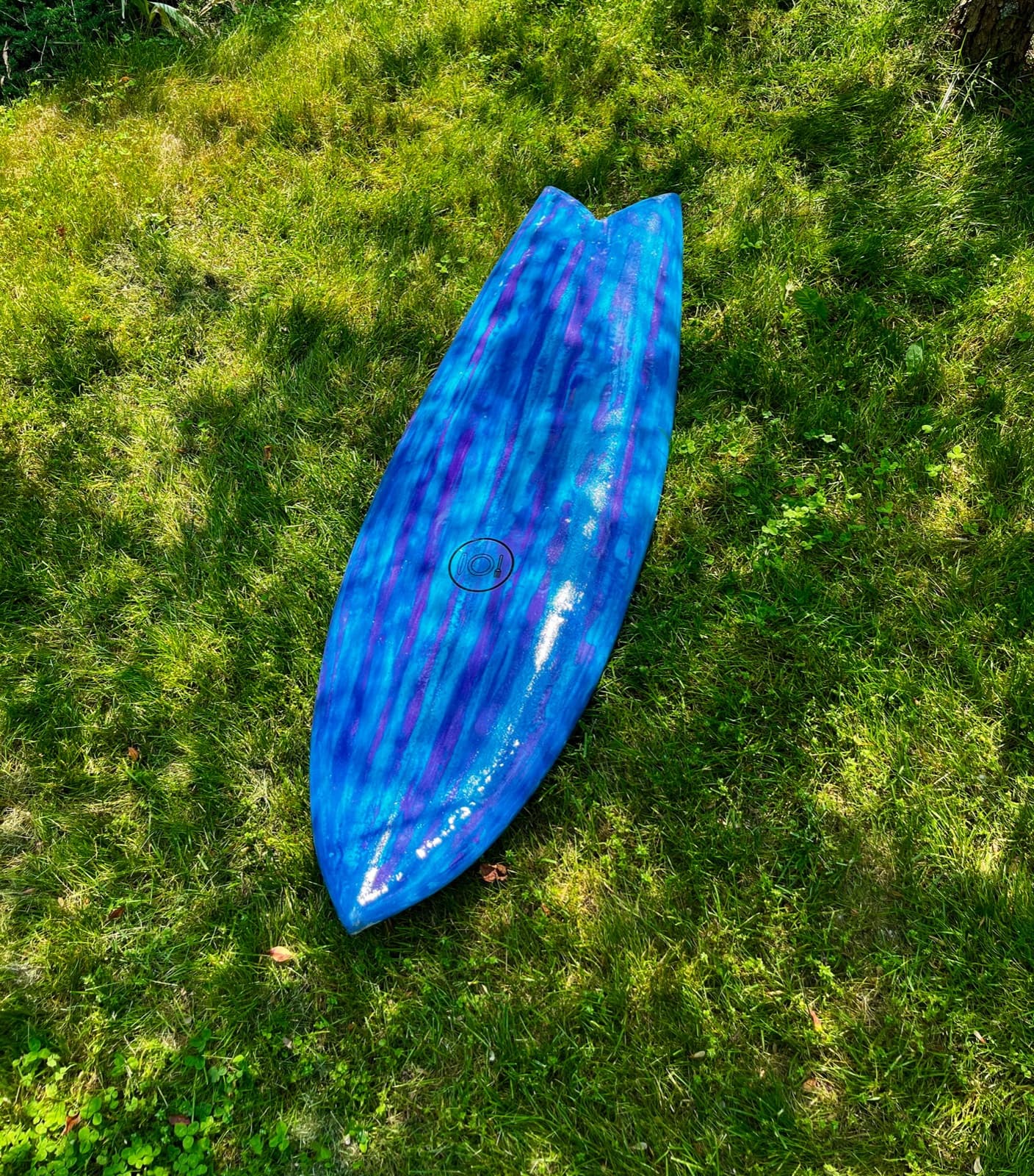 A blue tie-dyed surfboard lying on grass