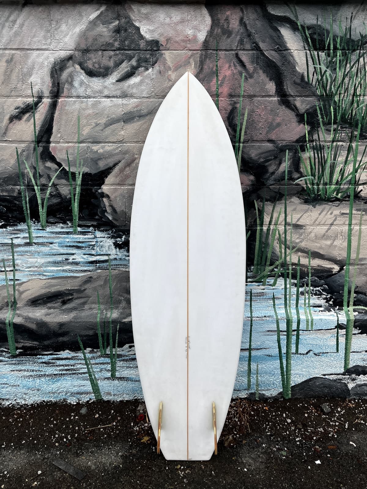 A plain white surfboard leaning against a painted mural