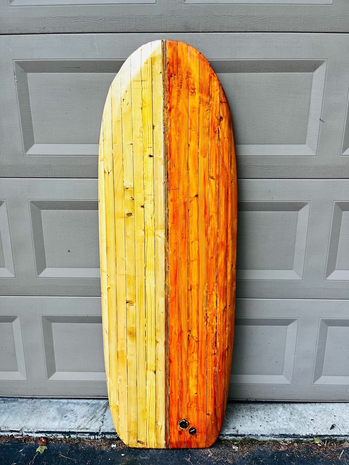 The Vino, a two-tone chambered wood surfboard, against a garage door